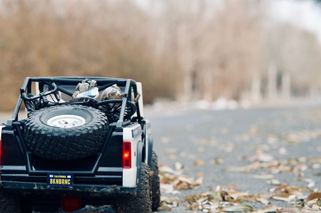Close-up of a toy SUV model on a leaf-covered forest road, showcasing back view and adventure themes.
