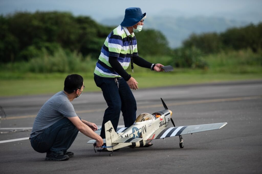 Two men preparing to launch a radio-controlled model airplane on an outdoor runway.