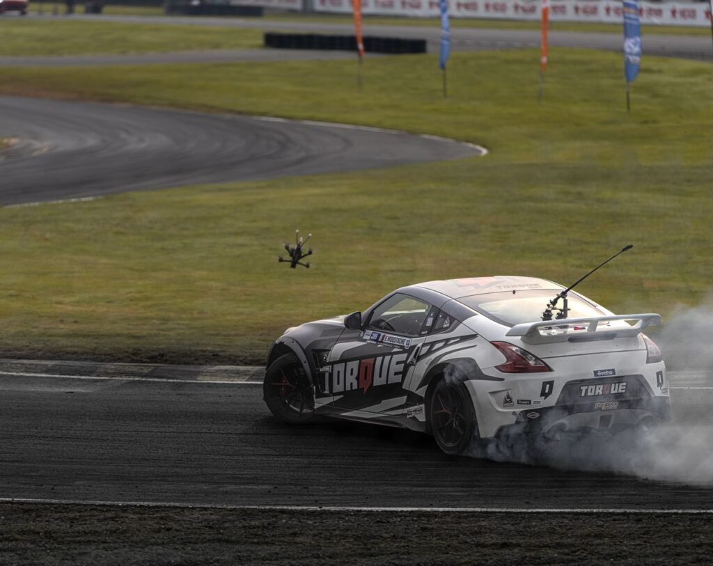 A sports car drifts at high speed on a race track, captured with DJI drone.