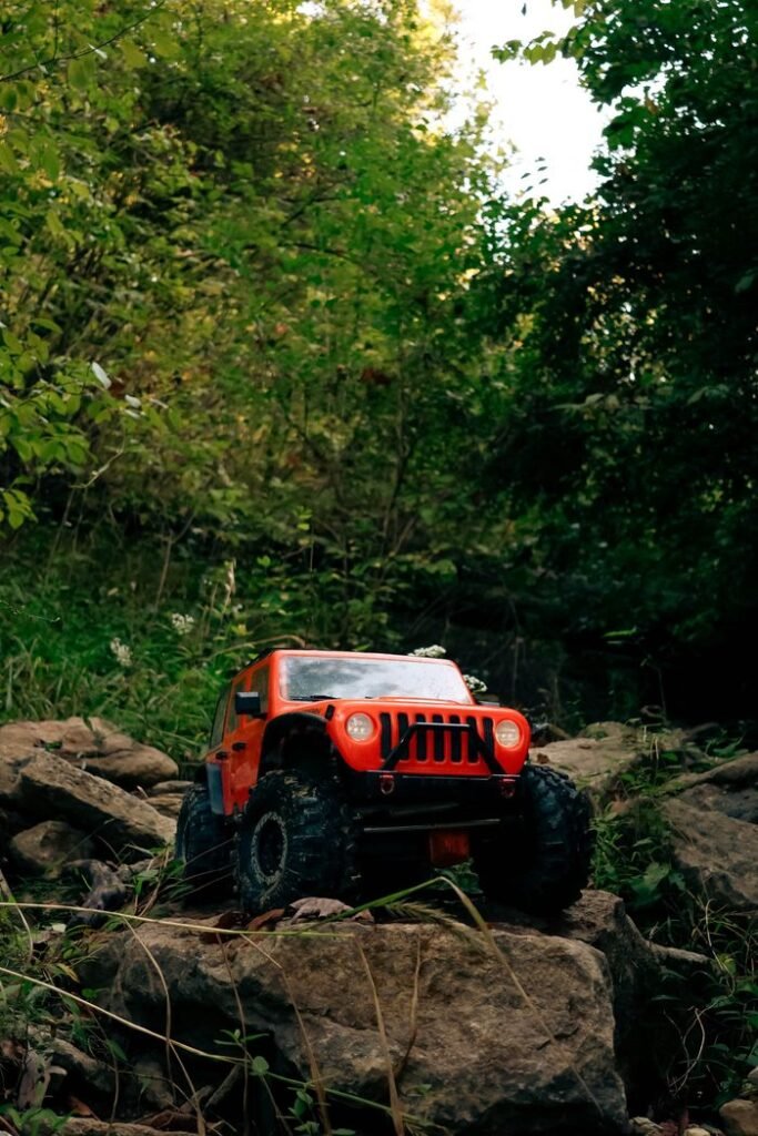 Orange remote control jeep navigating rocky outdoor terrain amidst lush greenery.