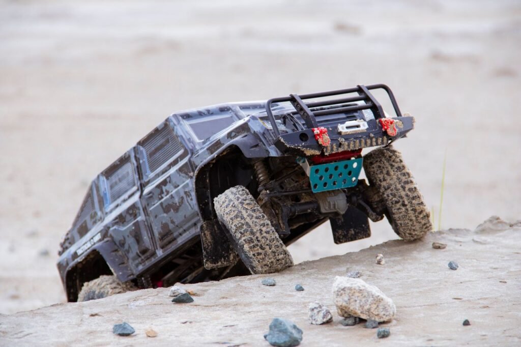 Close-up shot of a rugged RC toy car navigating sandy off-road terrain during daytime.
